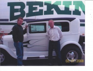 an old car and two men in front of a Bekins truck