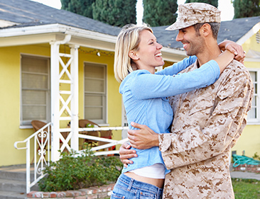 military couple hugging in front of their home
