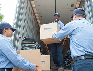 Wheaton employees carrying boxes out of moving van. 