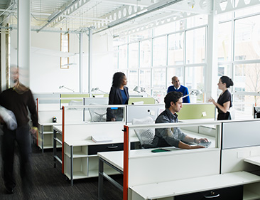 Employees moving around and talking in bright office space. 