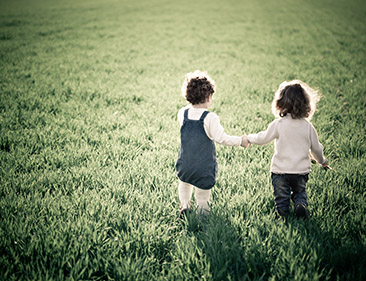 Young siblings walking in grass. 