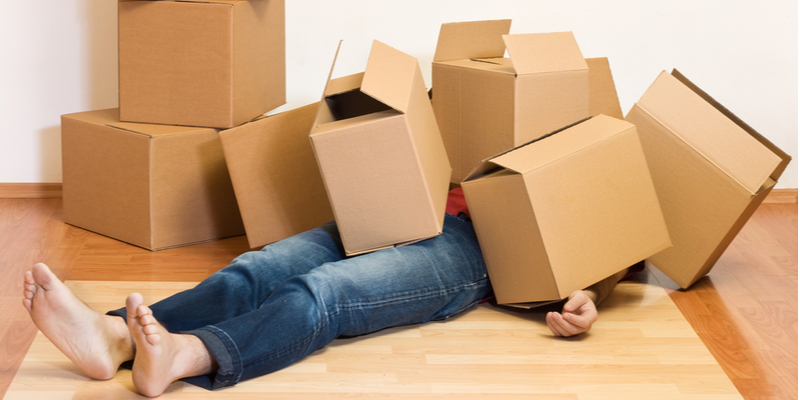 Sick or tired man laying face-up under a pile of cardboard moving boxes in an unfurnished room