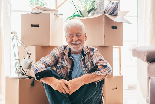 Elderly man surrounded by boxes and smiling.