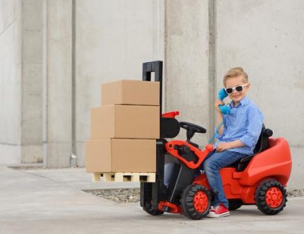 Kid in sunglasses driving a miniature forklift with moving boxes on it