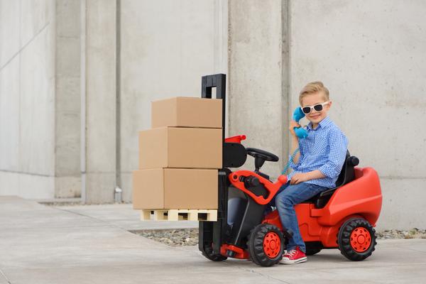 Kid in sunglasses driving a miniature forklift with moving boxes on it