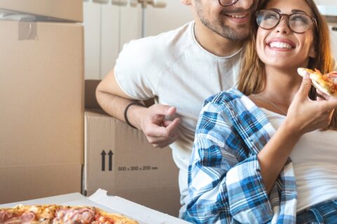 A couple eating pizza and smiling.