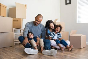 Family with young kids sitting by newly packed carboard boxes