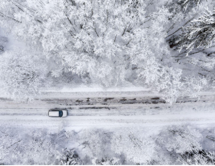 One vehicle driving through the winter snowy forest on a country road.