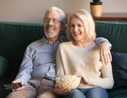 A smiling senior couple eating popcorn and watching tv on their couch.