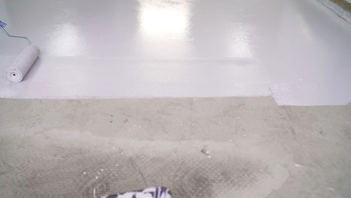 Painting a newly cleaned basement floor using a roller.