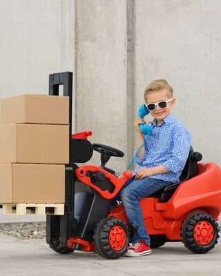 Kid in sunglasses driving a miniature forklift with moving boxes on it