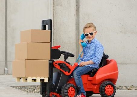 Kid in sunglasses driving a miniature forklift with moving boxes on it