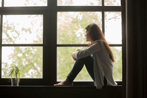 Woman sitting in a windowsill looking out the window.