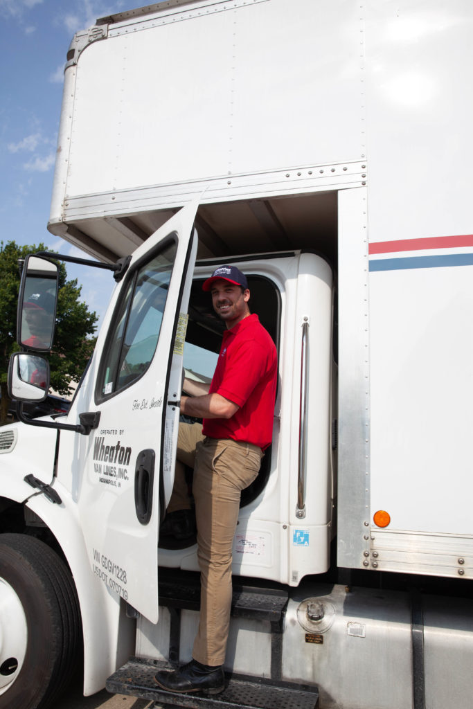 Wheaton moving driver climbing into front seat of Wheaton-branded moving truck. 