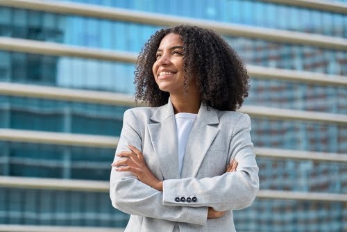 Happy young African American business woman standing in city looking away. Confident smiling confident professional businesswoman leader wearing suit thinking of success, dreaming of new goal outdoor.