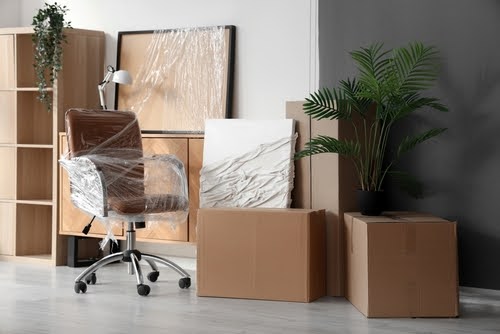 Interior of office with chair wrapped in stretch film and cardboard boxes on moving day