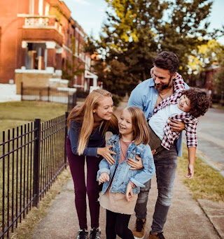 A family of four walks down a neighborhood sidewalk together.