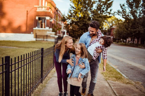 A family of four walks down a neighborhood sidewalk together.