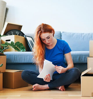 A young woman surrounded by moving boxes reviews financial documents.