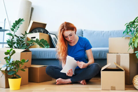 A young woman surrounded by moving boxes reviews financial documents.