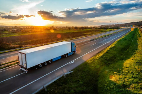 A moving van travels along a rural highway as the sun sets.